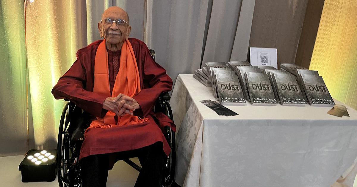 Indian actor, journalist, and author Noel De Souza sits next to copies of his debut novel, “Dust.”